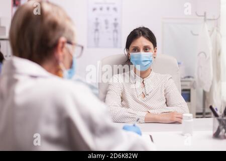 Ritratto del paziente preoccupato con maschera facciale contro il coronavirus durante la consultazione con il medico senior in ospedale. Foto Stock