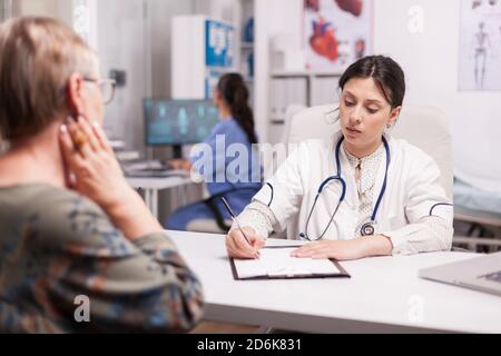 Dottore in ospedale scrivendo trattamento per la donna anziana durante l'esame. Infermiere con uniforme blu che lavora sul computer. Foto Stock