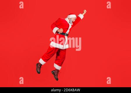 babbo natale positivo a tutta lunghezza che salta in alto e vola in aria come supereroe, in fretta per festeggiare le vacanze invernali. Riprese in studio al coperto Foto Stock