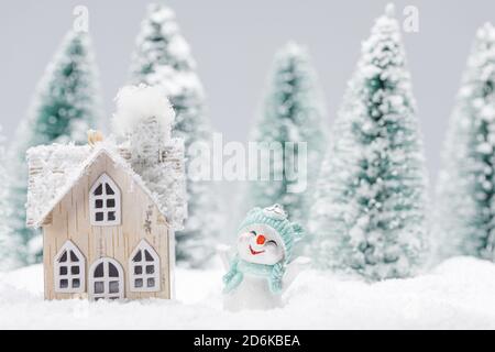 Piccolo pupazzo di neve decorativa con dono vicino casa in legno nel bosco di abeti sotto la neve Foto Stock