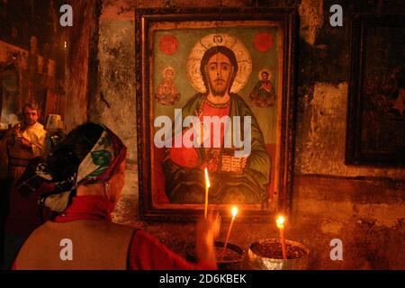 La chiesa ortodossa cristiana del XVIII secolo a Samburesti, Olt, Romania. Donna che illumina una candela ad una vecchia icona bizantina di Cristo Pantocratore. Foto Stock