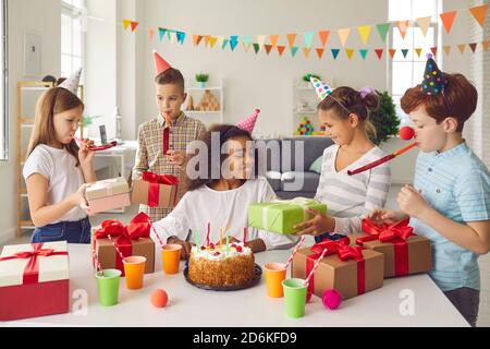 Gruppo di bambini in cappelli divertenti che danno regali di compleanno a. il loro amico in festa di divertimento a casa Foto Stock