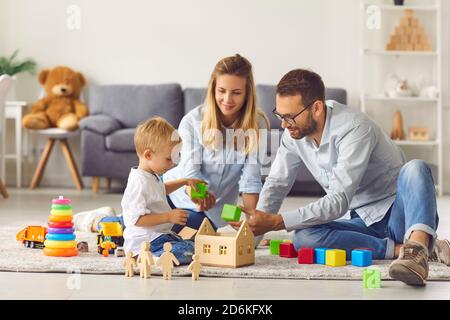Mamma, papà e bambino che giocano a casa con cubi colorati seduti sul pavimento tra giocattoli colorati. Foto Stock
