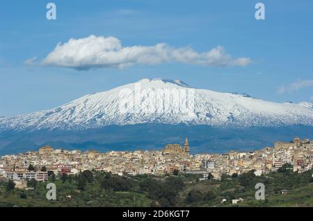 Vista delle dimore e della massiccia cattedrale nel villaggio di Regalbuto in Sicilia, sullo sfondo il vulcano Etna nevoso e grandi nuvole nel blu Foto Stock