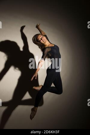 donna al buio esegue il salto ginnico, su uno sfondo bianco c'è un'ombra da una forma. Fotografia da studio. Foto Stock