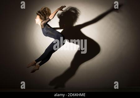 donna al buio esegue il salto ginnico, su uno sfondo bianco c'è un'ombra da una forma. Fotografia da studio. Foto Stock