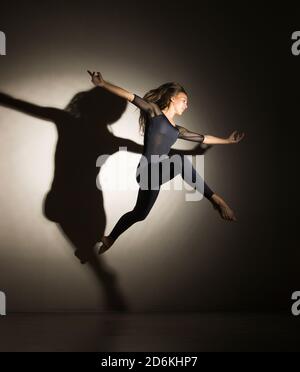 donna al buio esegue il salto ginnico, su uno sfondo bianco c'è un'ombra da una forma. Fotografia da studio. Foto Stock