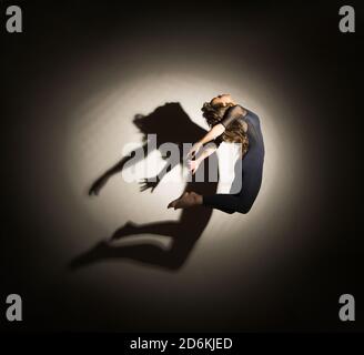 donna al buio esegue il salto ginnico, su uno sfondo bianco c'è un'ombra da una forma. Fotografia da studio. Foto Stock