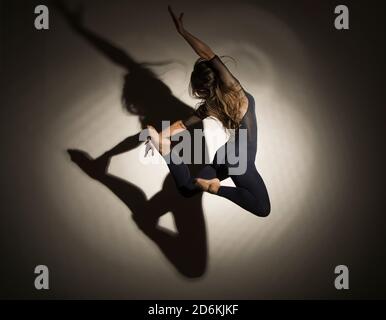 donna al buio esegue il salto ginnico, su uno sfondo bianco c'è un'ombra da una forma. Fotografia da studio. Foto Stock