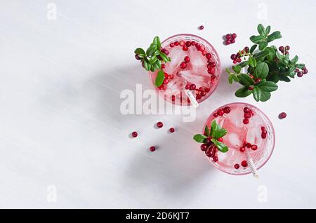 Cocktail rosa di bacche fredde con mirtillo, ghiaccio e foglie verdi in fascio di sole su tavolo di legno bianco, spazio copia, vista dall'alto. Foto Stock