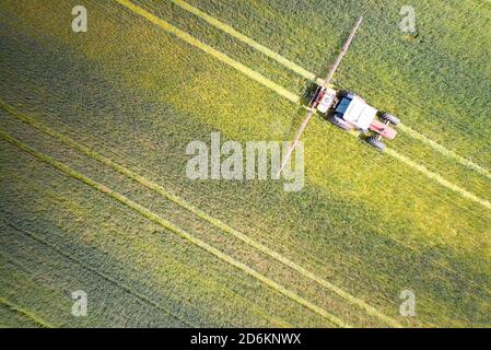 Punto di vista del drone di un trattore che spruzza su un campo coltivato. Foto Stock