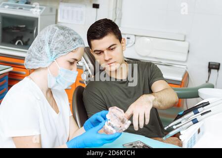 Il dentista femminile mostra il trattamento imminente sulla mascella artificiale. Paziente soddisfatto nella sedia del dentista. Foto Stock