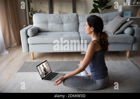 Donna sportiva motivata che indossa abbigliamento sportivo che pratica yoga, utilizzando un computer portatile Foto Stock