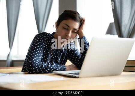 Annoiata donna d'affari indiana addormentata seduta al banco del lavoro Foto Stock