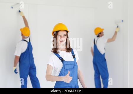 Lavoratore femminile dà i pollici di fronte a due pittori Foto Stock