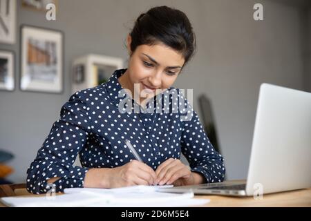 La scrittura delle note indiane di businesswoman fa il rapporto finanziario sedersi vicino al laptop Foto Stock