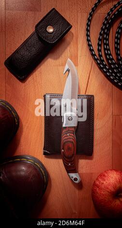 Un coltello e stivali su sfondo di legno Foto Stock