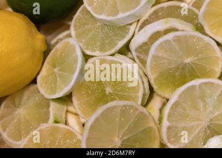 limone intero e lime intero adagiato su un letto di limoni e lime a fette Foto Stock