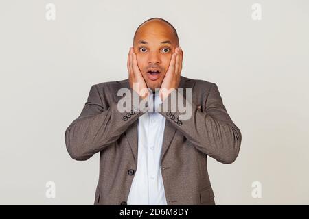 Scioccato giovane uomo d'affari afro-americano che esprime sorpresa e stupore, toccando il viso e piegando le labbra, si alza in uno stupore e occhiali alla macchina fotografica, essendo impressionato Foto Stock