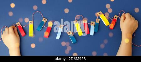 Autorimessa decorativa artigianale di carta con luci colorate in mani di bambino su sfondo blu classico, felice anno nuovo 2021, volantino di natale allegro, bann Foto Stock