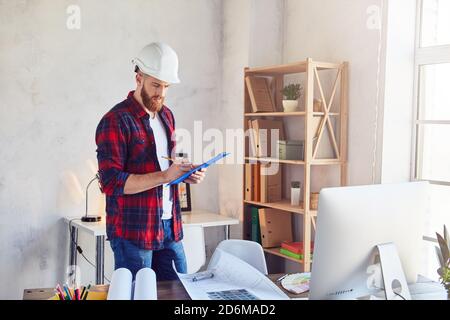 Giovane uomo in casco guardando il progetto del nuovo progetto e prendendo appunti. Progettazione e progettazione architettonica Foto Stock