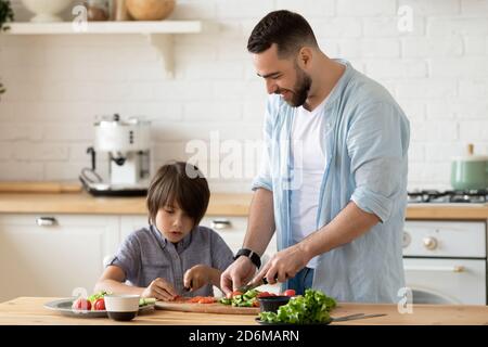 Giovane padre premuroso insegnando il piccolo figlio a cucinare l'insalata Foto Stock