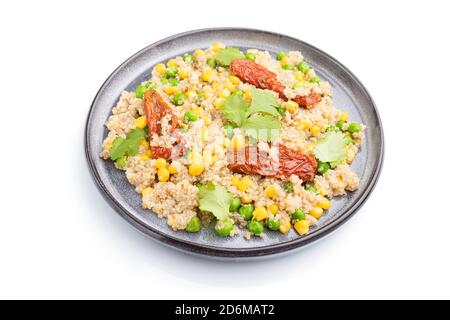 Porridge di quinoa con piselli verdi, mais e pomodori secchi su piastra di ceramica isolata su fondo bianco. Vista laterale, primo piano. Foto Stock
