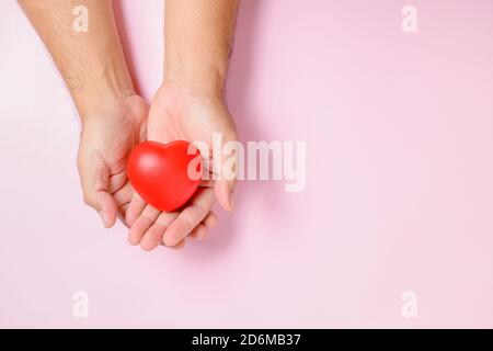 Mano uomo che tiene il cuore rosso su sfondo rosa, donazione, felice carità volontaria, responsabilità sociale CSR, giornata del cuore del mondo, giornata mondiale della salute, mondo Foto Stock