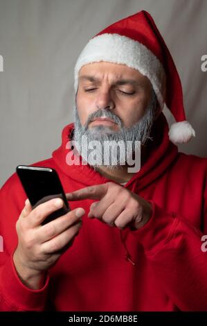 Babbo Natale digita qualcosa sul suo cellulare e guarda sospetto Foto Stock