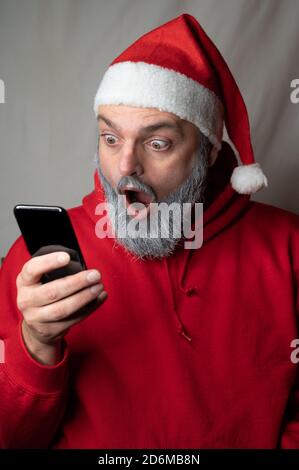 Babbo Natale guarda un cellulare con la bocca ampia apertura Foto Stock