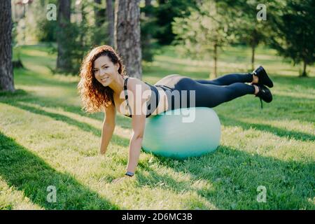 Concetto di sport, ricreazione, fitness e stile di vita sano. Brunette sportiva giovane donna europea in abbigliamento attivo si appoggia sulla palla fitness, rende fisico ex Foto Stock