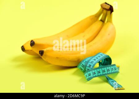 Il nastro di misurazione in colore turchese accanto al mucchio di banane, isolata luce su sfondo giallo. Concetto di vitamina E della dieta a basso contenuto calorico cibo Foto Stock