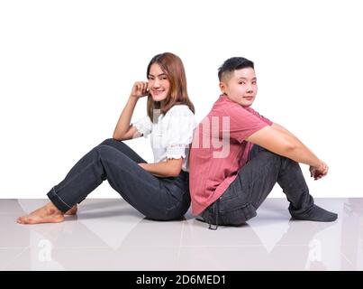 Due donne sorridenti giovani ragazze e felicità Tomboy amici seduti torna indietro su pavimento in piastrelle in casa con bianco sfondo Foto Stock