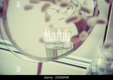Fiori soffici in vaso e profumo, specchio riflettente, stile retrò astratto, foto in tonalità vintage. Foto Stock