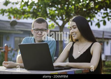 Due giovani studenti seduti nel parco che parlano e studiano sul computer portatile Foto Stock