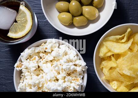 Popcorn, olive, patatine e bevande su un tavolo testurizzato blu. Prospettiva Foto Stock
