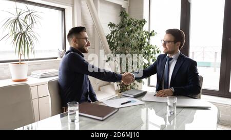 Due uomini d'affari sorridenti e misti che scuotono le mani in ufficio. Foto Stock