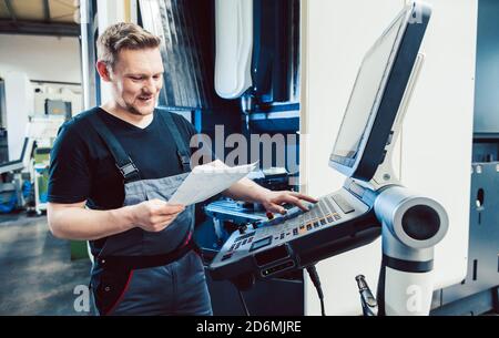 Operatore in officina industriale che programma una macchina cnc Foto Stock