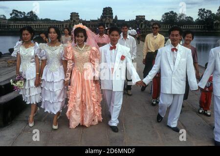 Un gruppo di sposi in abito rosa, e sposo, bridesmaids e migliori uomini in bianco sulla strada rialzata Angkor Wat al Parco storico di Angkor, Cambogia Foto Stock