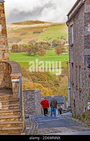 Persone che camminano per la strada di Mill Brow in cumbrian città mercato di Kirkby Lonsdale con una vista di Lo Yorkshire Dales Beyond Foto Stock