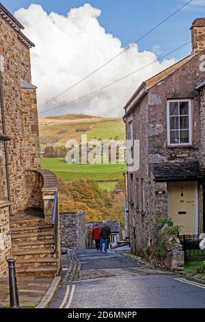 Persone che camminano per la strada di Mill Brow in cumbrian città mercato di Kirkby Lonsdale con una vista di Lo Yorkshire Dales Beyond Foto Stock