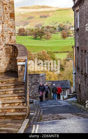 Persone che camminano per la strada di Mill Brow in cumbrian città mercato di Kirkby Lonsdale con una vista di Lo Yorkshire Dales Beyond Foto Stock