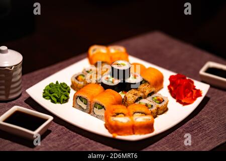 Serve appetitosi sushi su piatto bianco nel cafe. Primo piano di gustosi panini di sushi con wasabi e zenzero nel ristorante tradizionale giapponese. Foto Stock