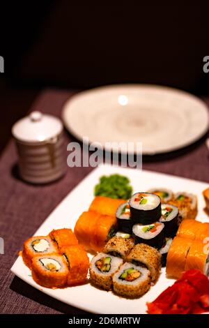 Serve appetitosi sushi su piatto bianco nel cafe. Primo piano di gustosi panini di sushi con wasabi e zenzero nel ristorante tradizionale giapponese. Foto Stock