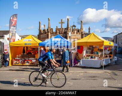 Uomo in bicicletta passato bancarelle di mercato nella piazza del mercato in La città Cumbriana di Kirkby Lonsdale Inghilterra UK Foto Stock