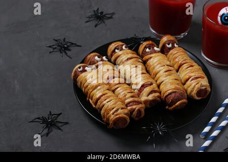 Mummie di salsiccia e succo di pomodoro per la festa di Halloween su un piatto scuro. Idea di cibo divertente per i bambini. Foto Stock