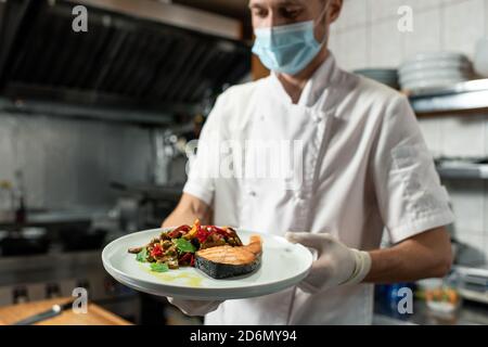 Giovane chef professionista che tiene piatto con salmone fritto e verdure guarnire Foto Stock