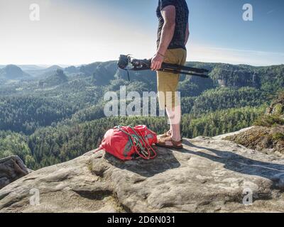 Turista con treppiede e macchina fotografica in mano guardare la natura selvaggia da alta scogliera affilata in montagna. Foto Stock
