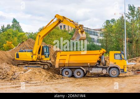 Il carrello giallo e l'escavatore caricano il terreno con sabbia durante la strada costruzione in area urbana Foto Stock