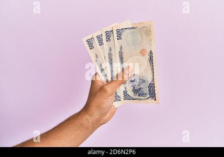 Mano ispanica che tiene 5000 yen giapponesi su sfondo rosa isolato. Foto Stock